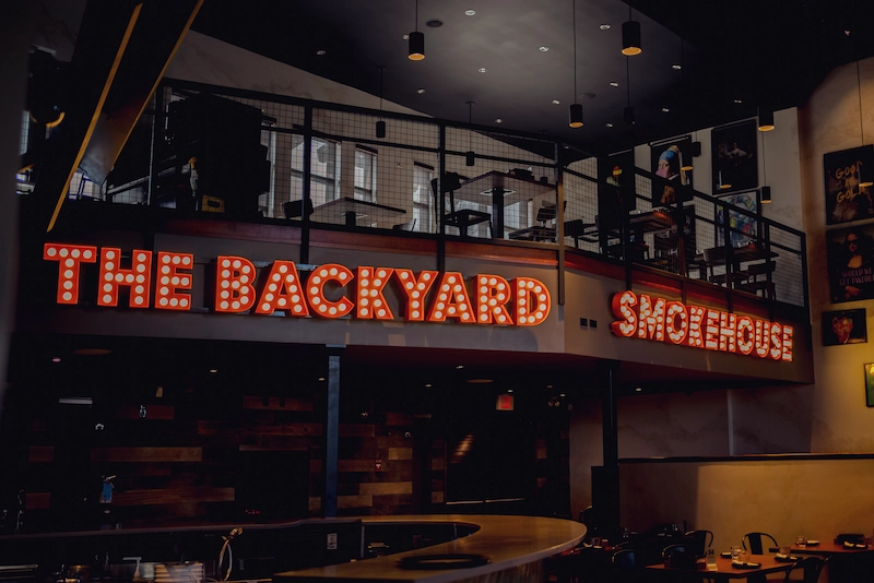 Backyard Smokehouse Edmonton illuminated marquee sign and two-level dining room interior
