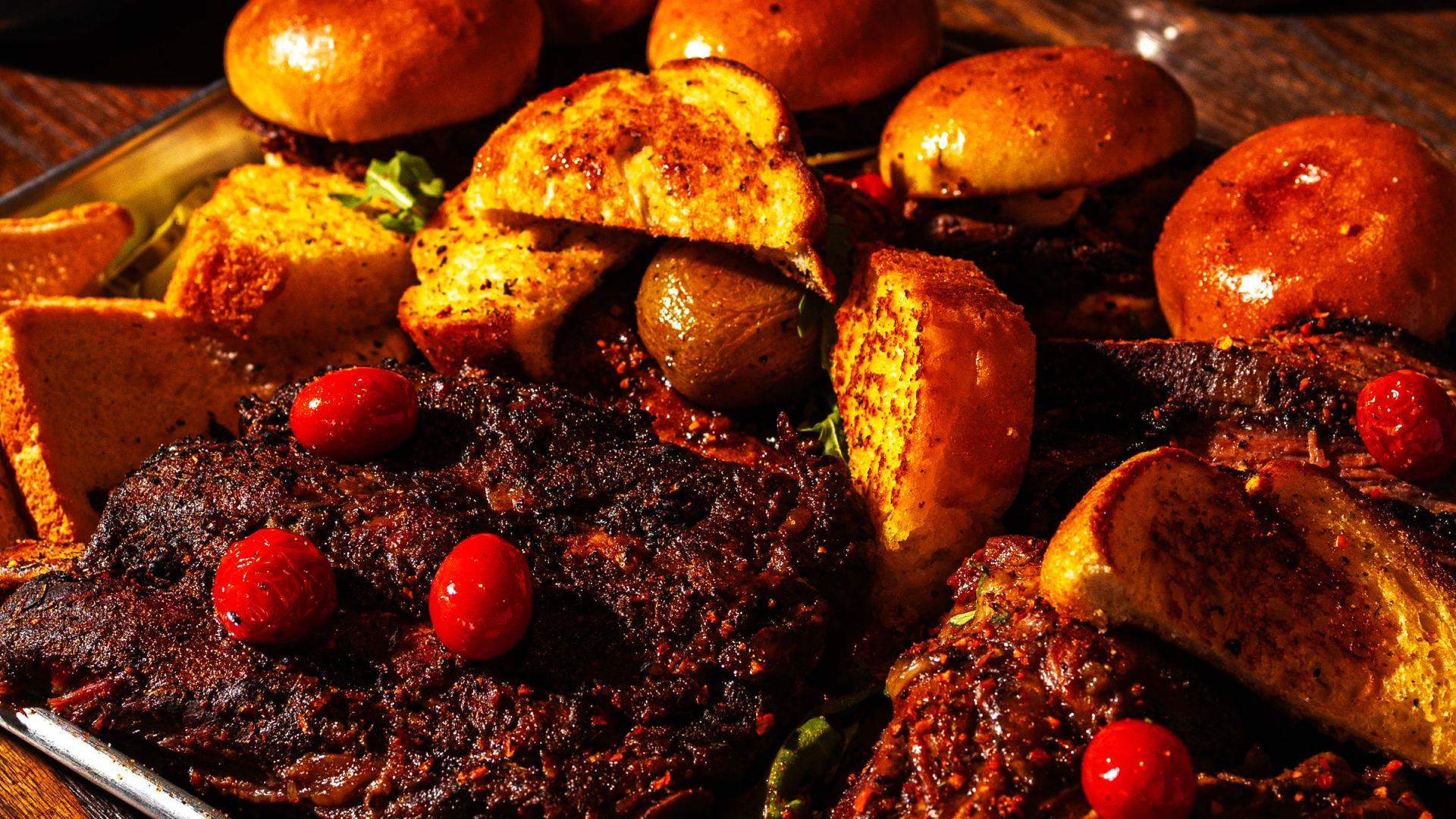 Close-up of a Backyard Smokehouse BBQ platter with smoked meat, roasted potatoes, brioche buns and cherry tomatoes