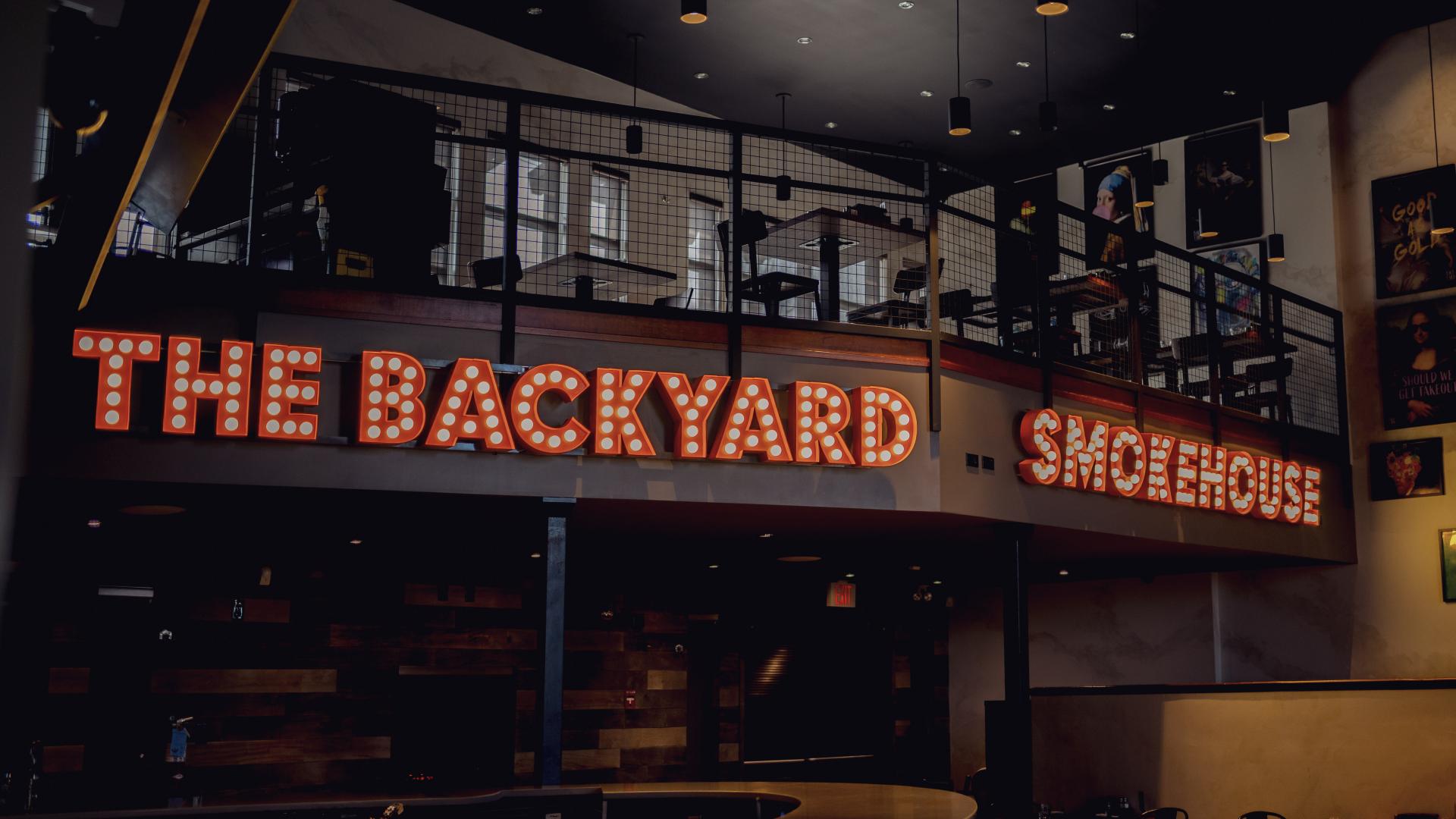 Illuminated The Backyard Smokehouse marquee sign inside the restaurant dining area