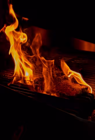 Backyard Smokehouse Edmonton open grill with high flames cooking beef low and slow